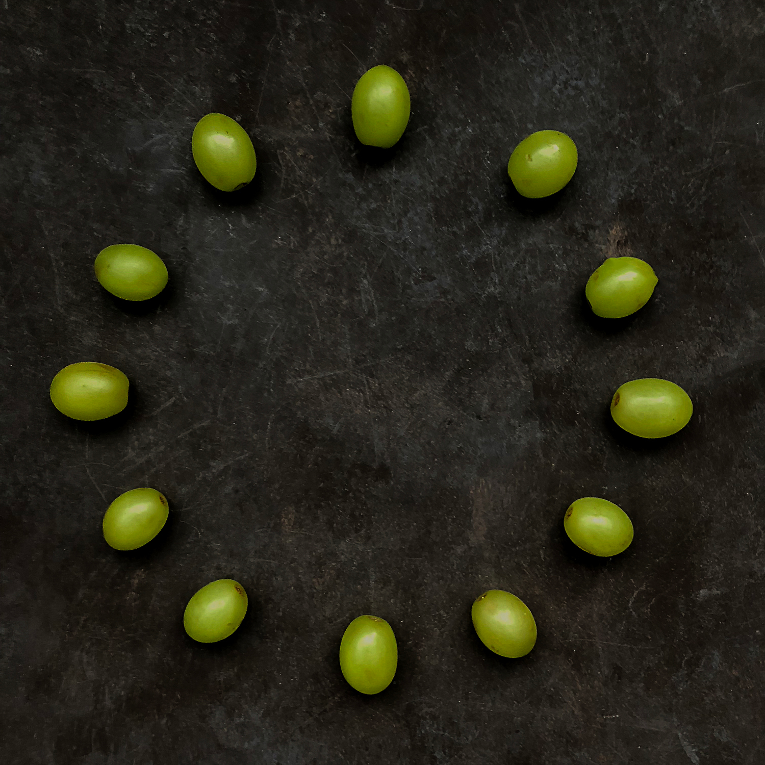 12 grapes laid out on a dark background with each grape representing a number on a clock face.